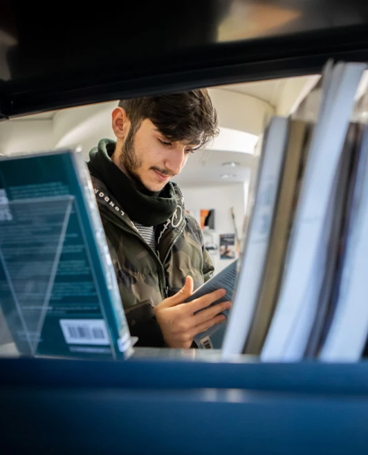 Student browsing and reading a book between shelves in the East End Campus library at Glasgow Kelvin College. Student browsing and reading a book between shelves in the East End Campus library at Glasgow Kelvin College.